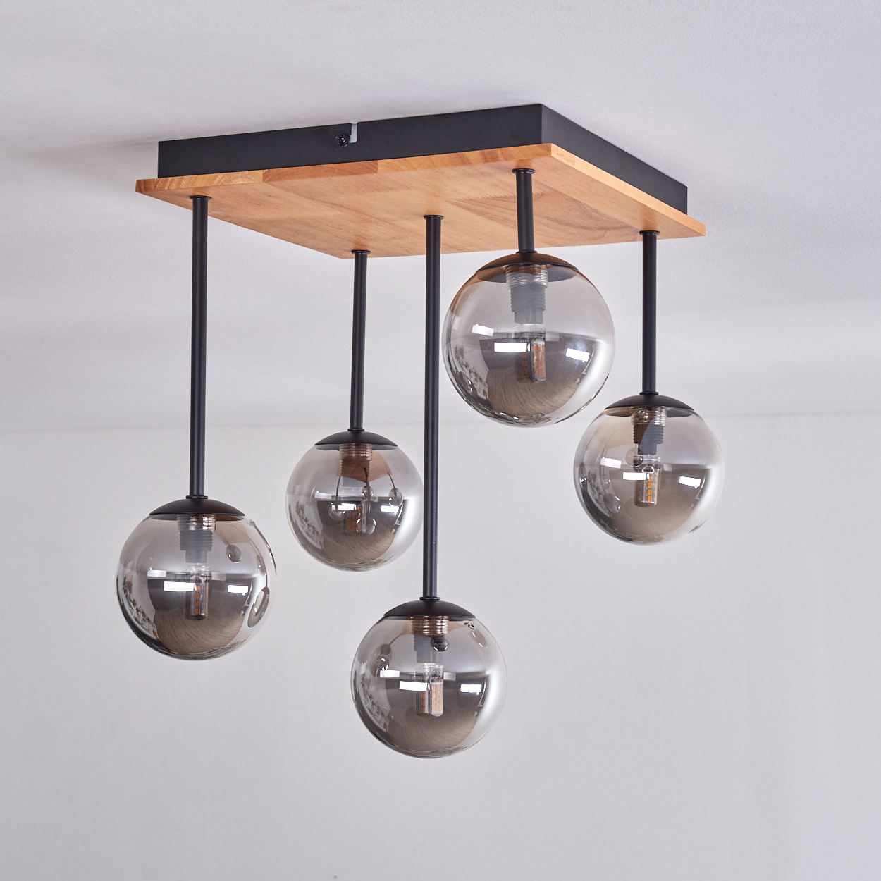 Eine moderne Deckenleuchte mit fünf Glaskugelschirmen. Die Leuchte hat eine Holzbasis mit schwarzen Metallstangen.