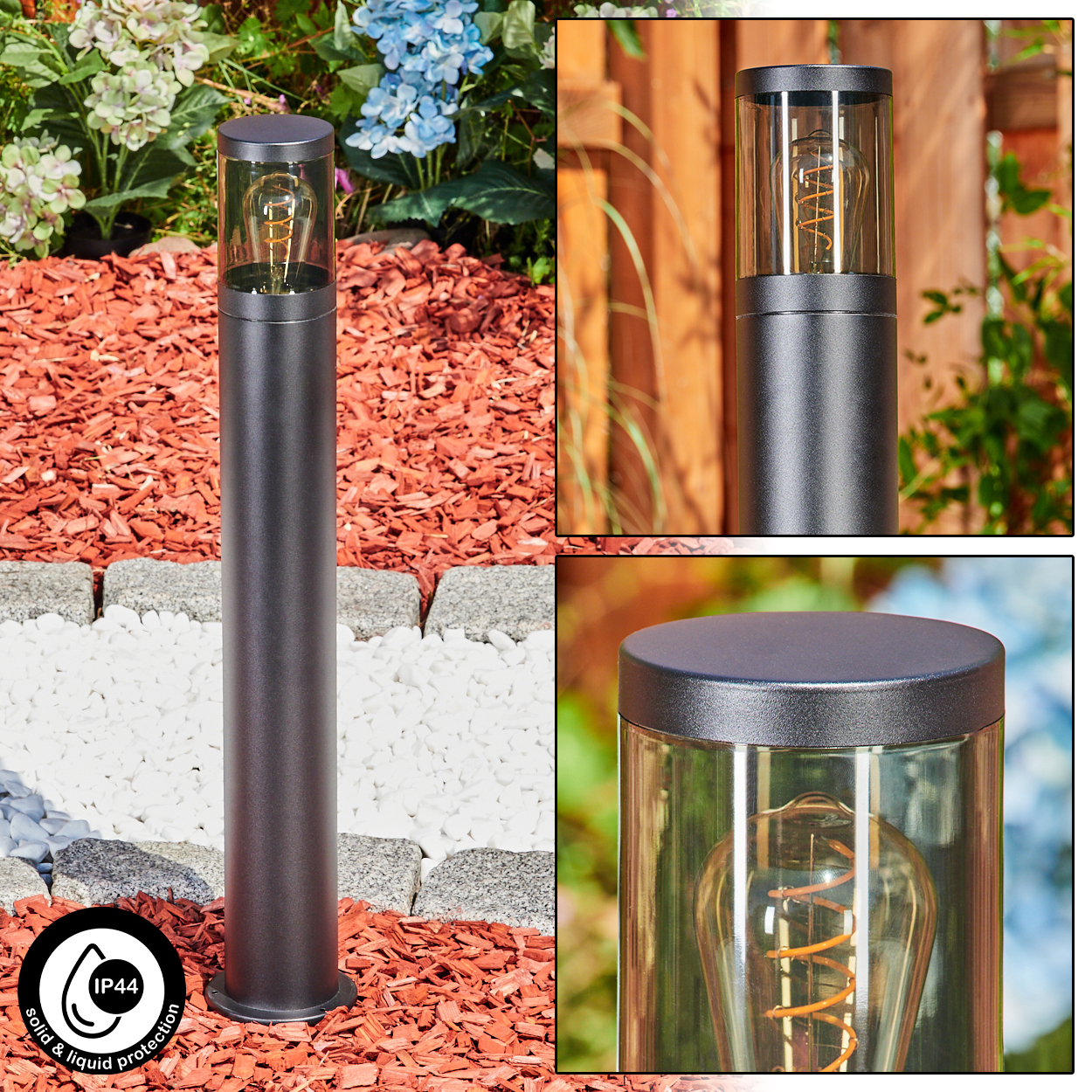 Eine schwarze Außenlampe mit Glasabdeckung und einer Glühbirne im Vintage-Stil, in einem Garten mit roter Mulche und Blumen.