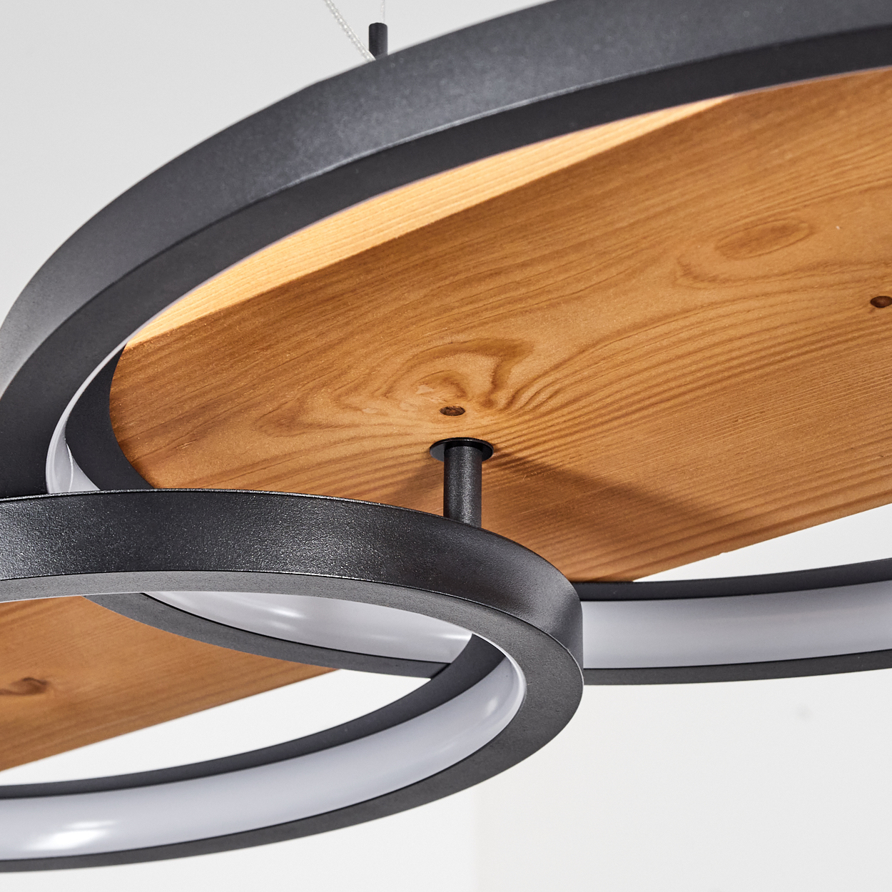 Nahaufnahme einer modernen Deckenleuchte. Sie hat schwarze Metallringe mit Holz und weißen Lichtern. Der Hintergrund ist weiß.
