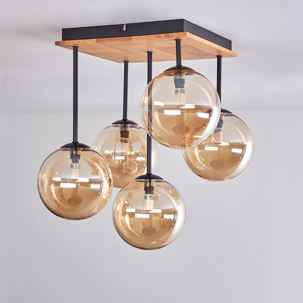 Eine moderne Deckenleuchte mit fünf bernsteinfarbenen Glaskugelschirmen hängt an einer quadratischen Holz- und schwarzen Metallhalterung.