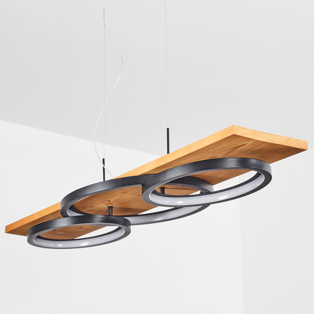 Eine moderne Leuchte mit drei schwarzen kreisförmigen Lichtern und einem Holzbrett, das von der Decke hängt.