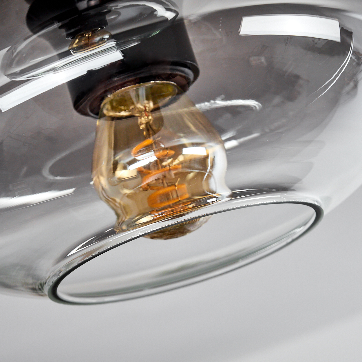 Nahaufnahme einer Leuchte. Ein klarer Glasschirm umgibt eine glühende, warm getönte Glühbirne. Die Leuchte hat schwarze und braune Details.