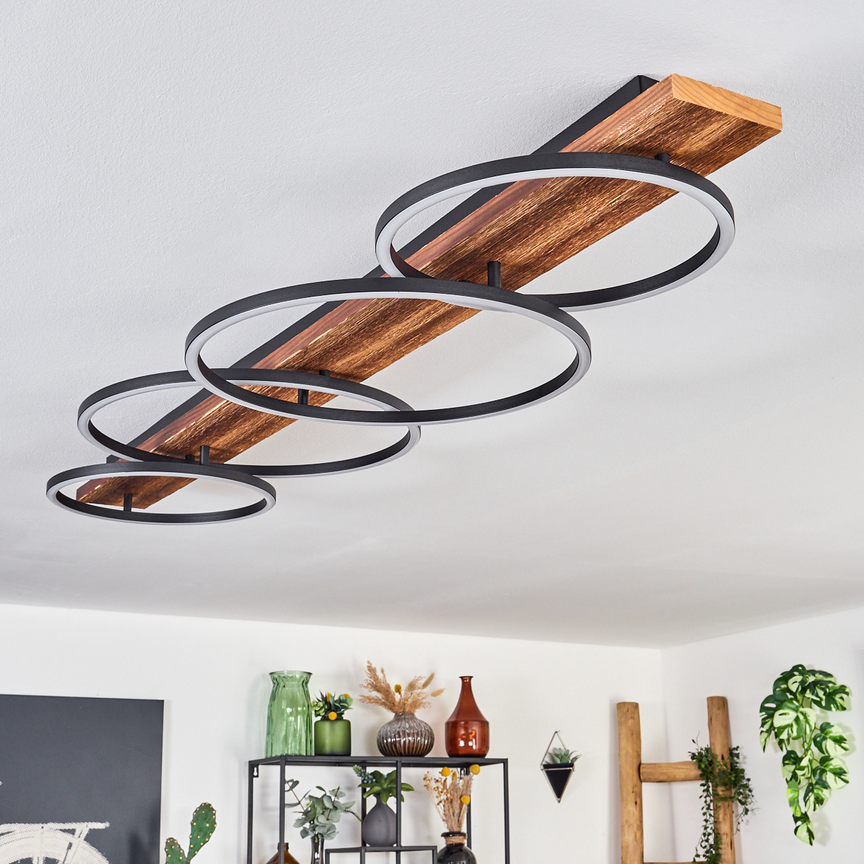 Moderne Deckenleuchte mit schwarzen Ringen und Holzbalken. Darunter Regale mit Vasen und Pflanzen.