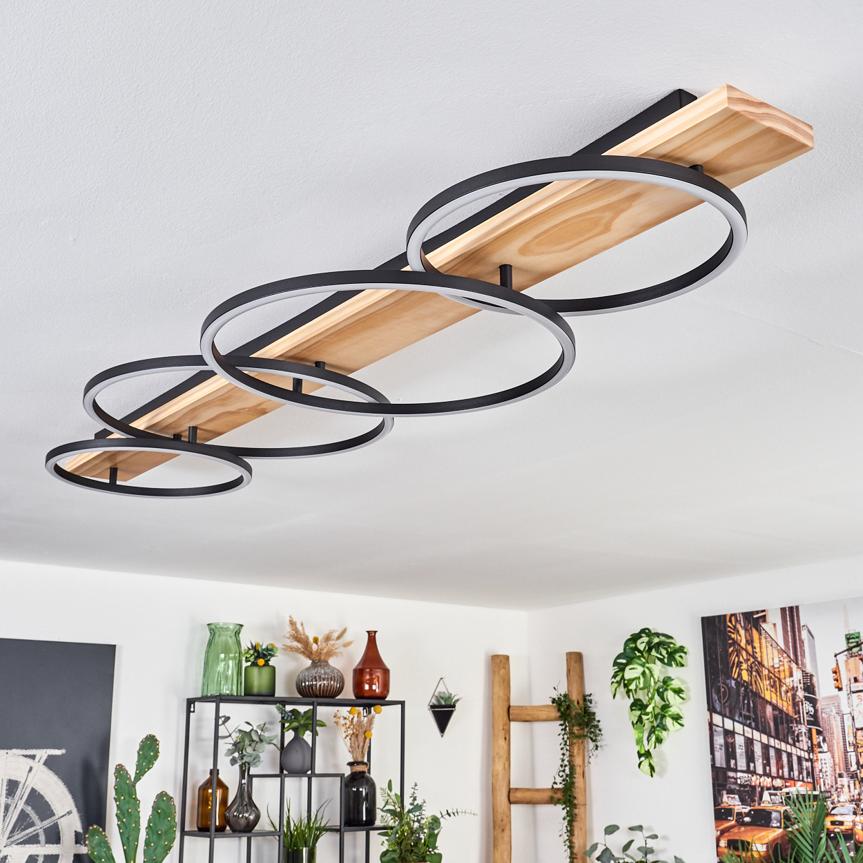 Eine moderne Deckenlampe mit schwarzen kreisförmigen Lichtern ist auf einem Holzbrett montiert. Der Raum hat Dekoration, Pflanzen und ein Stadtbildgemälde.
