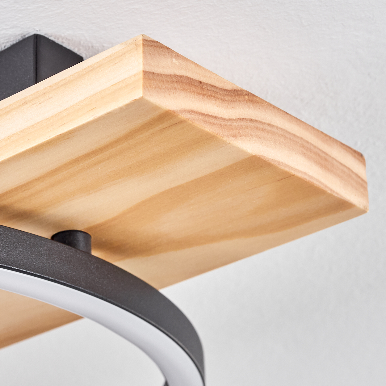 Nahaufnahme eines Holzregals. Darunter eine gebogene, dunkle Metallkonstruktion mit hellem, weißem LED-Licht. Der Hintergrund ist eine weiße Wand.