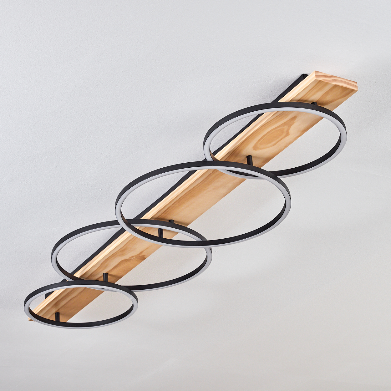 Deckenleuchte mit schwarzen Ringen und einem Holzbalken. Der Hintergrund ist eine weiße Decke.