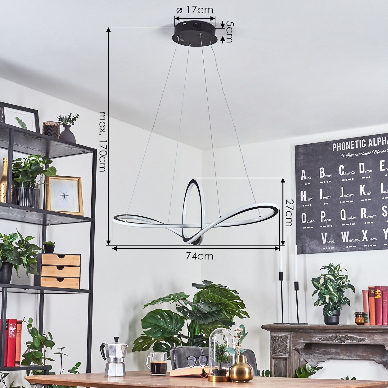 Eine moderne Hängelampe hängt über einem Holztisch. Es ist von Pflanzen, einem Regal und einem phonetischen Alphabet-Poster umgeben.