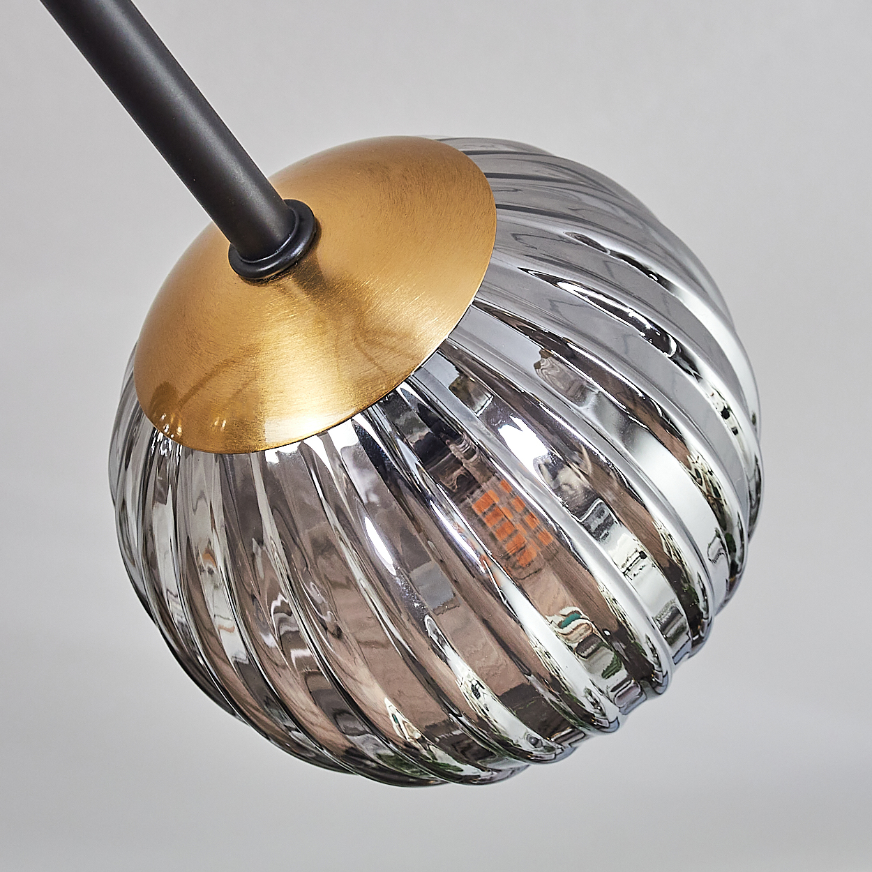 Eine moderne Lampe mit einem kreisförmigen Metallelement in Gold und einem transparenten, gerippten, kugelförmigen Glasschirm.