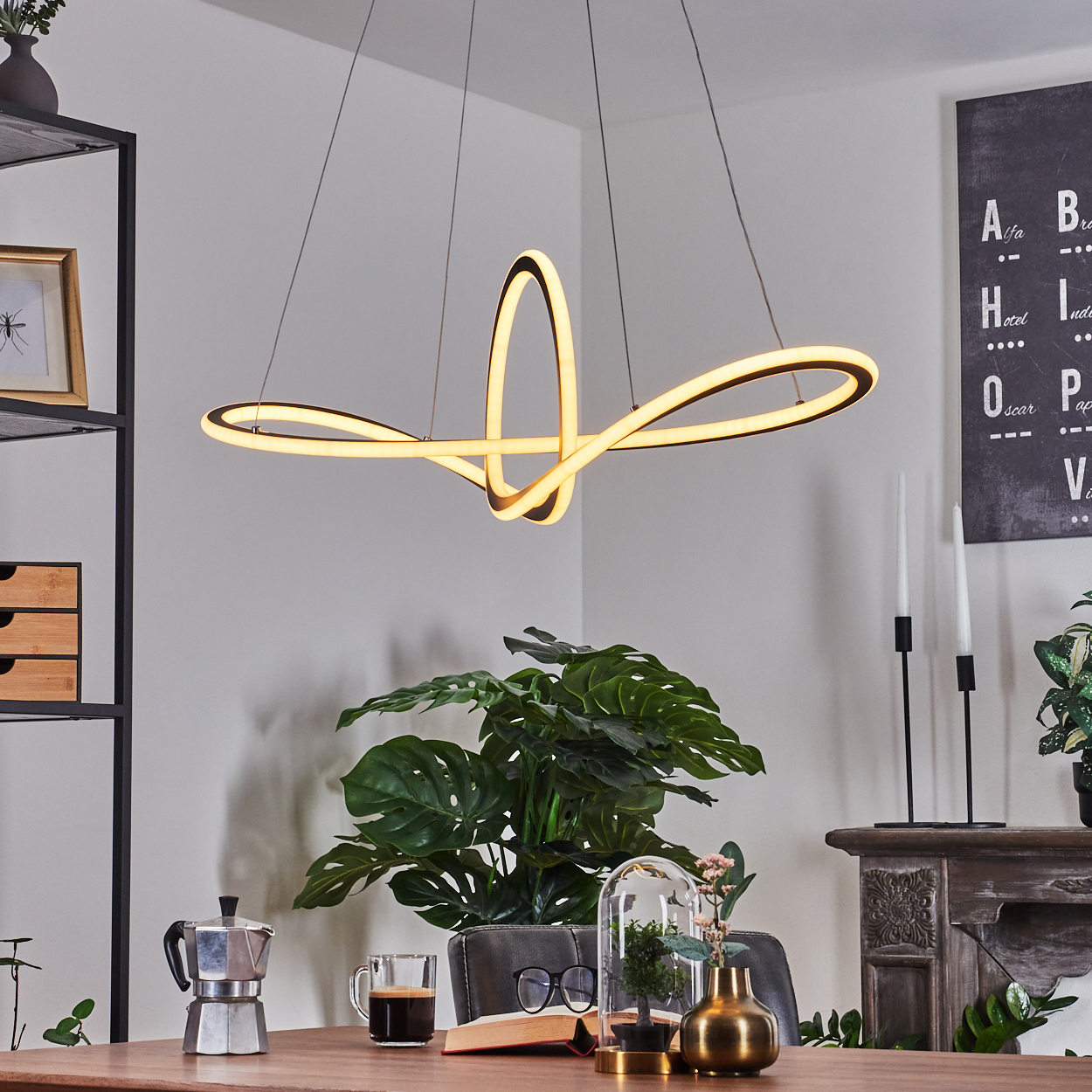 Ein modernes Esszimmer mit einer großen Leuchte, einem Tisch mit Kaffee, Pflanzen und Dekoration. Eine Tafel mit Buchstaben an der Wand.