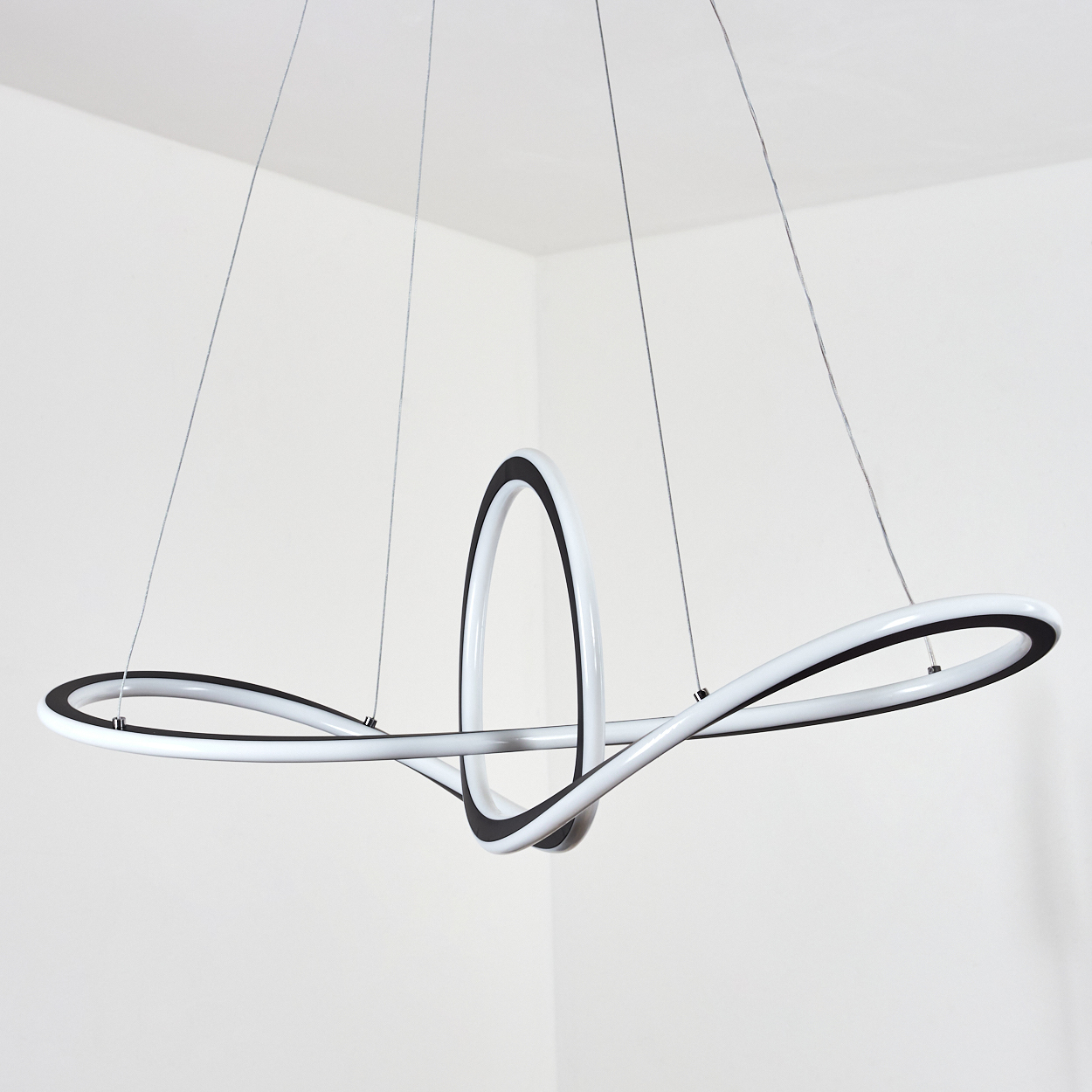 Eine moderne, weiß-schwarze Hängelampe hängt von der Decke. Es ist ein Schleifendesign mit dünnen Kabeln. Die Wände sind weiß.