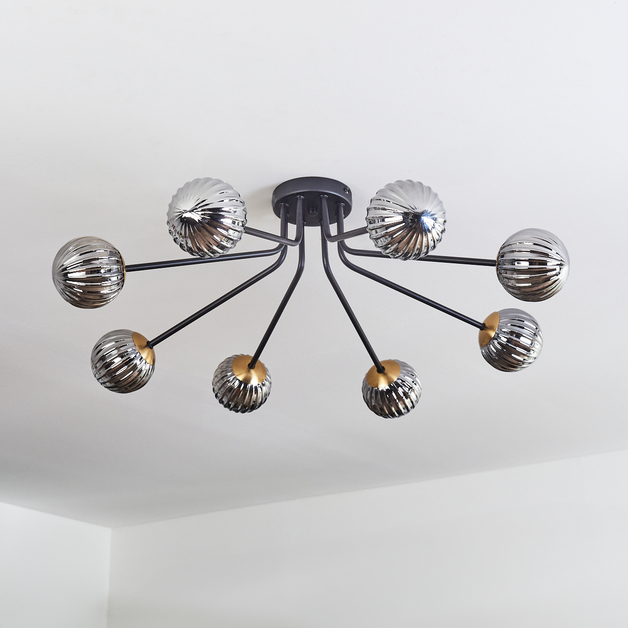 Moderne Deckenleuchte mit acht silbernen Kugelschirmchen an schwarzen Armen. Die Decke ist weiß.