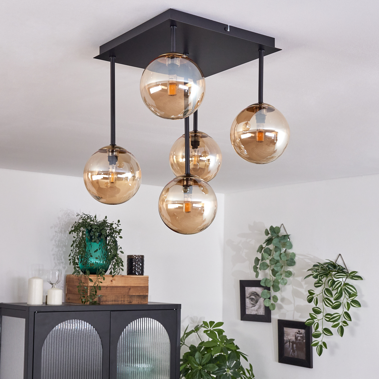 Eine moderne Deckenleuchte mit fünf kugelförmigen Lampen, schwarzem Sockel und Schrank mit Deko und Pflanzen.