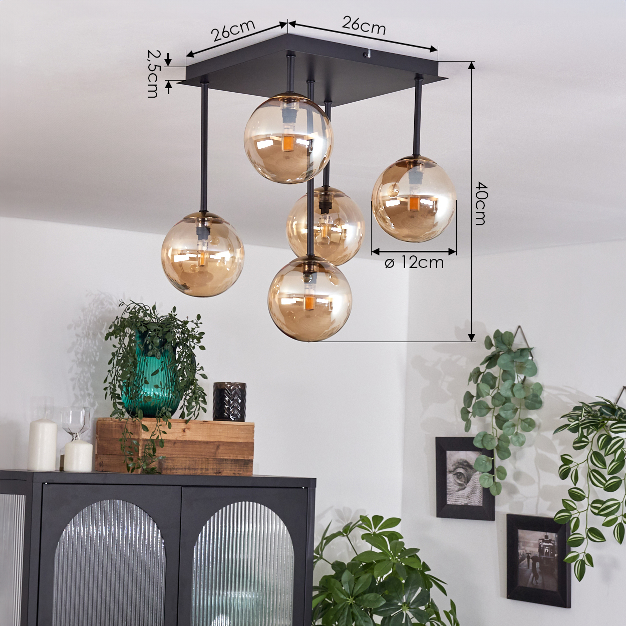 Eine schwarze Deckenlampe mit fünf kugelförmigen, bernsteinfarbenen Glasschirmen hängt. Darunter sind ein Schrank, Pflanzen und Dekorationsartikel zu sehen.