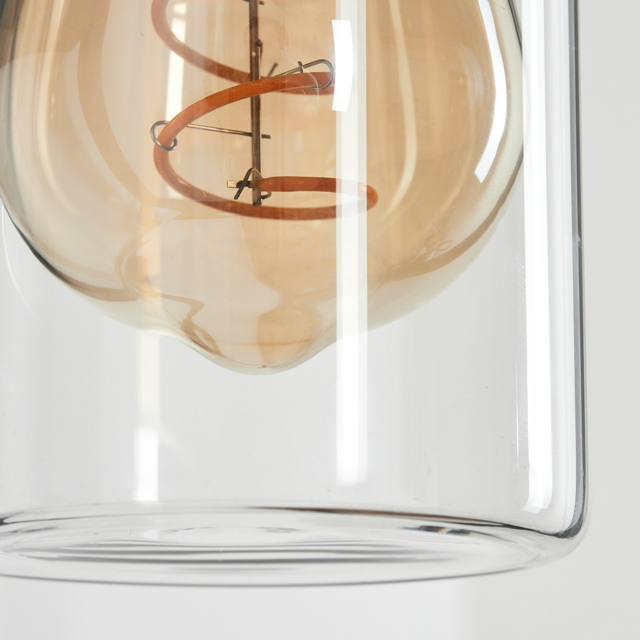 Nahaufnahme einer Glühbirne in einem transparenten Glasgehäuse. Die Glühbirne ist bernsteinfarben und hat einen Wendelfaden.