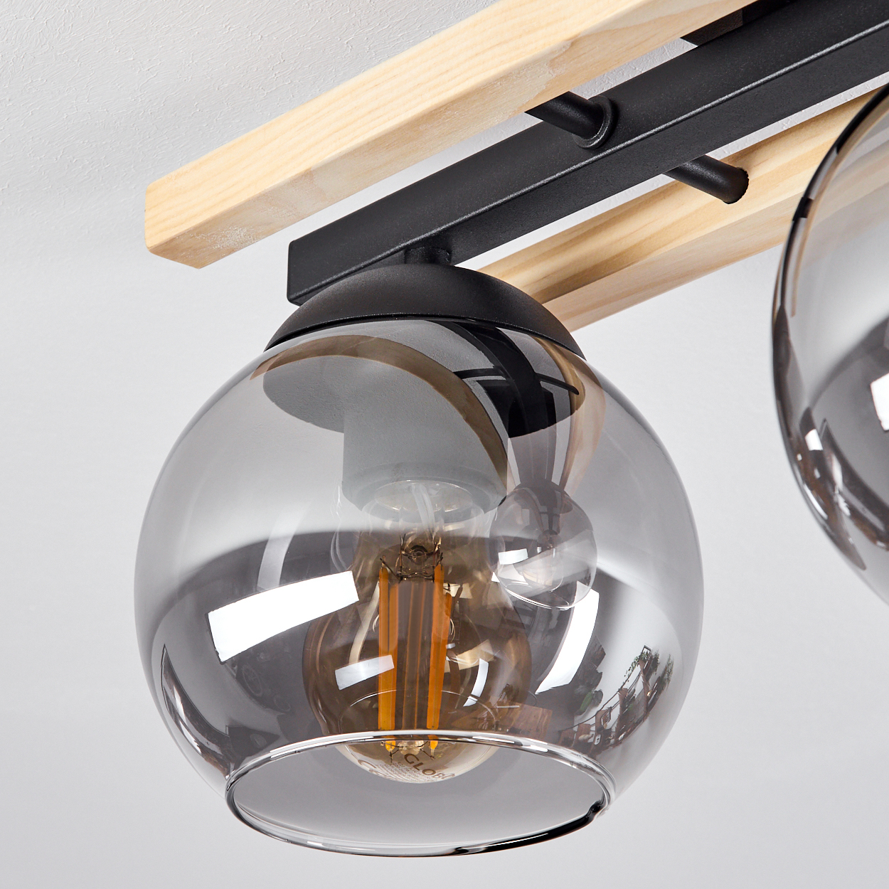 Nahaufnahme eines modernen Kronleuchters mit Glaskugeln. Das Gerät hat Holzbalken und schwarze Metallstützen, sichtbare Glühbirnen.