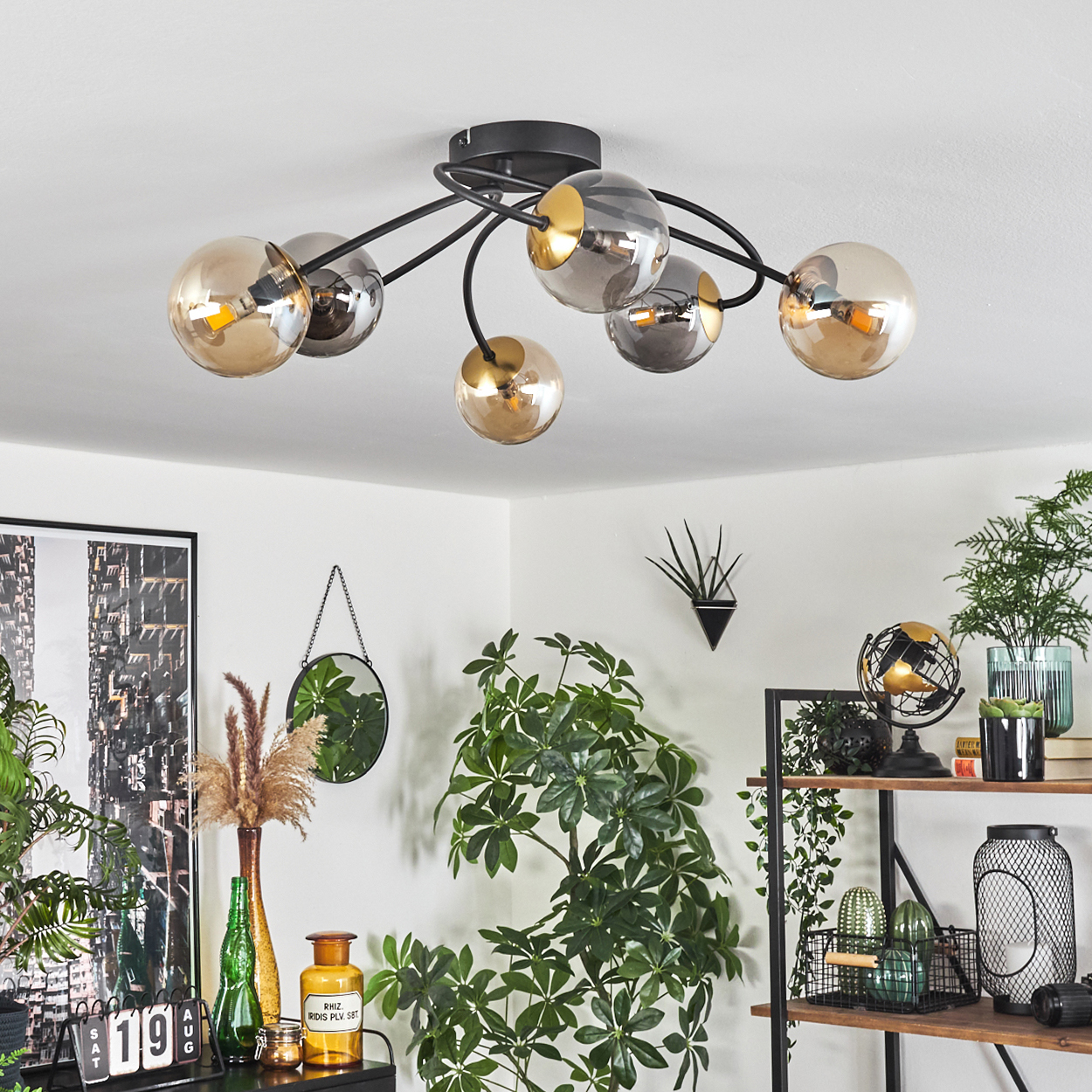 Ein modernes Wohnzimmer mit Deckenlampe mit Glaskugeln, Pflanzen und dekorativen Elementen. Das Farbschema ist neutral mit grünen Akzenten.