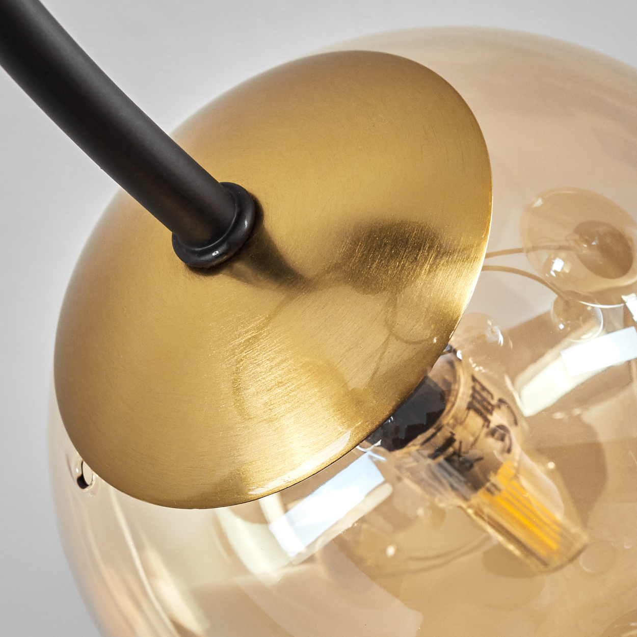 Nahaufnahme einer modernen Lampe. Sie hat einen goldfarbenen Metallschirm und eine klare Glaskugel mit einer sichtbaren Glühbirne.