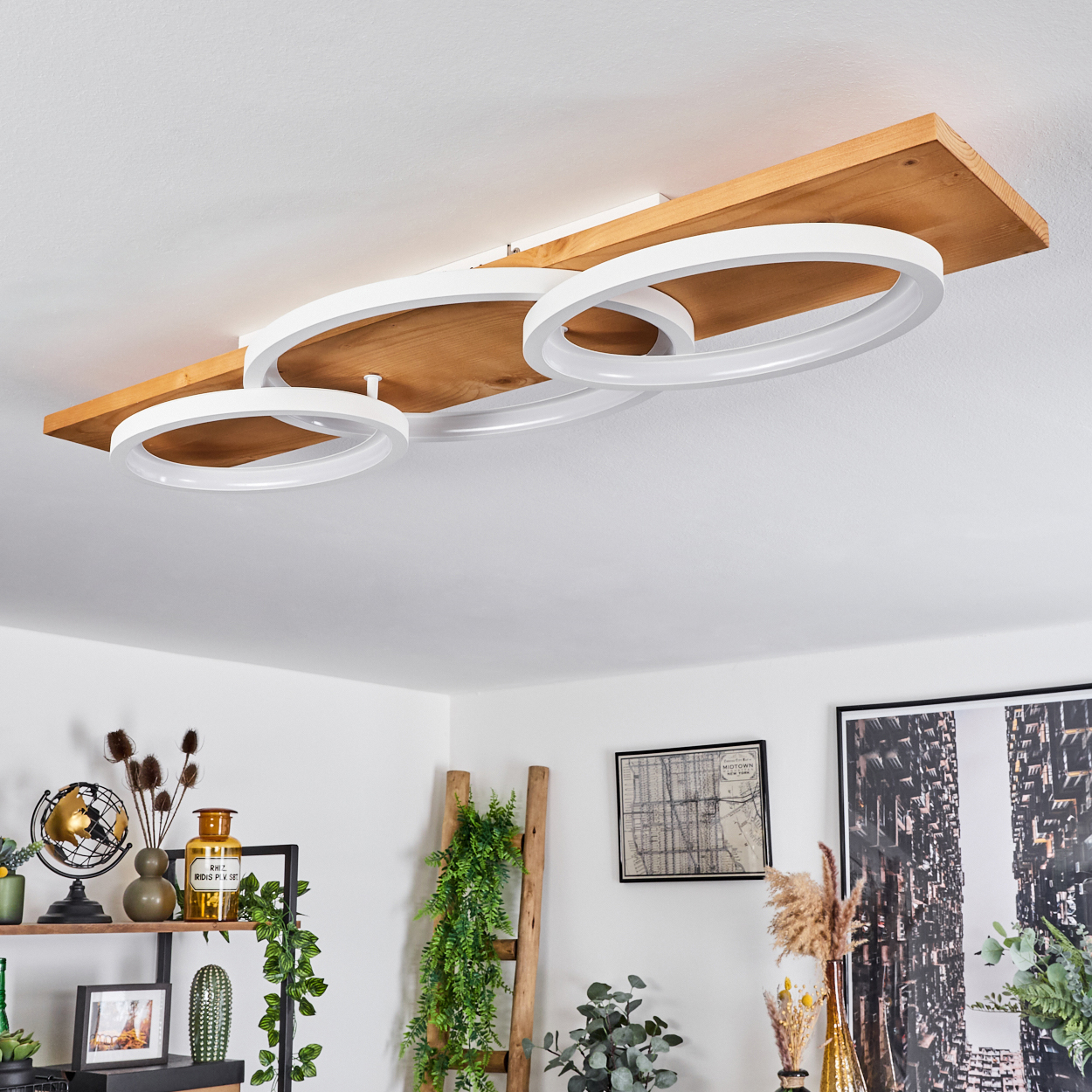 Eine moderne Deckenleuchte mit weißen kreisförmigen Lichtern auf einem Holzbrett. Dekorationsartikel und Pflanzen sind im Raum sichtbar.