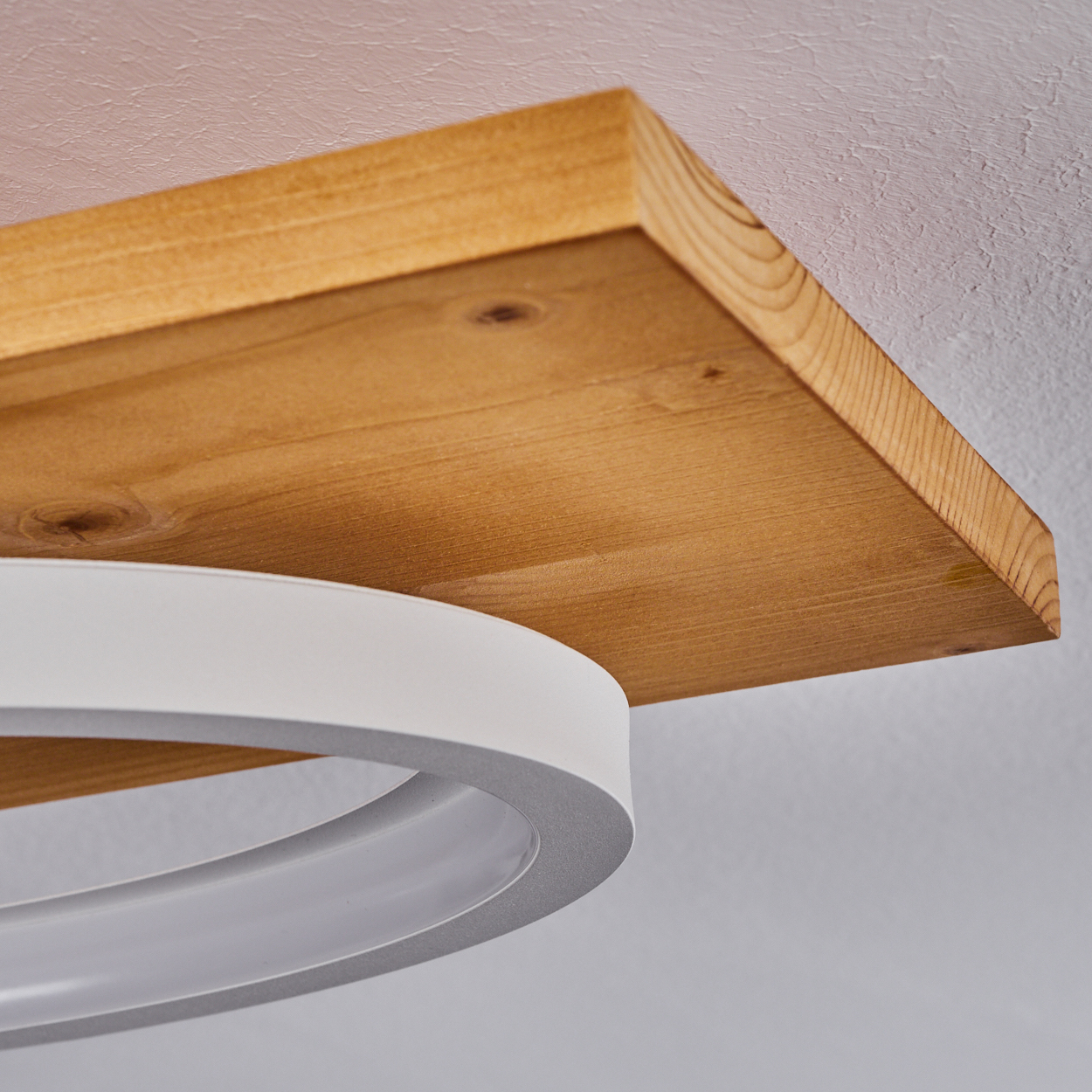 Ein Holzregal mit sichtbarer Holzmaserung liegt über einer weißen, oval geformten Leuchte. Der Hintergrund ist eine weiße Wand.