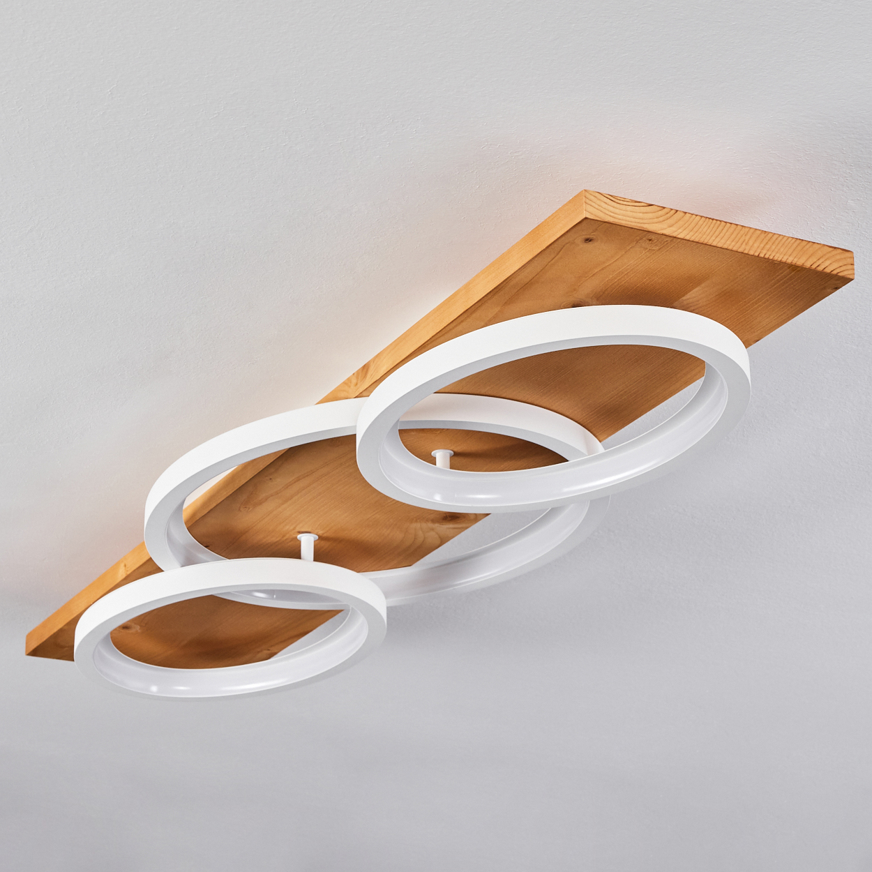 Eine Deckenleuchte mit drei weißen, kreisförmigen Lichtern, die an einem Holzbrett befestigt sind. Der Hintergrund ist eine weiße Decke.