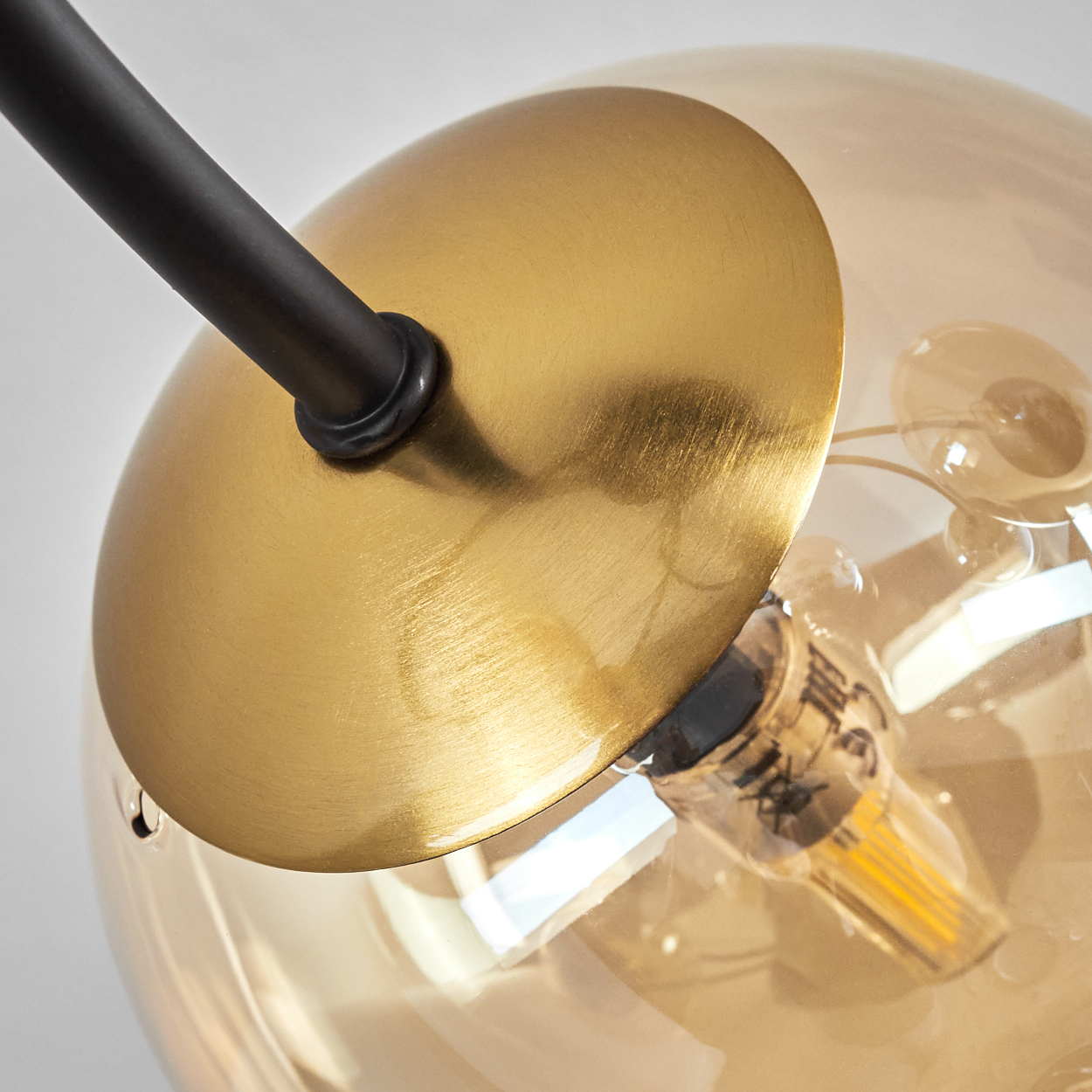 Nahaufnahme einer modernen Leuchte. Eine goldene Scheibe ist an einer klaren Glaskugel befestigt. Eine schwarze Stange erstreckt sich von der Leuchte.