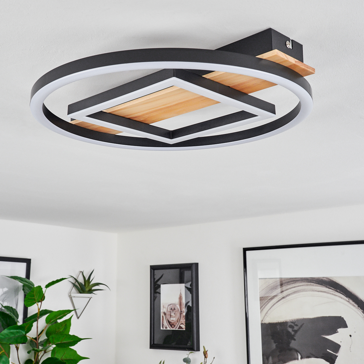 Eine Deckenleuchte mit kreisförmigem Design, schwarzem Rahmen und Holzpaneel. Der Raum hat weiße Wände und gerahmte Bilder.