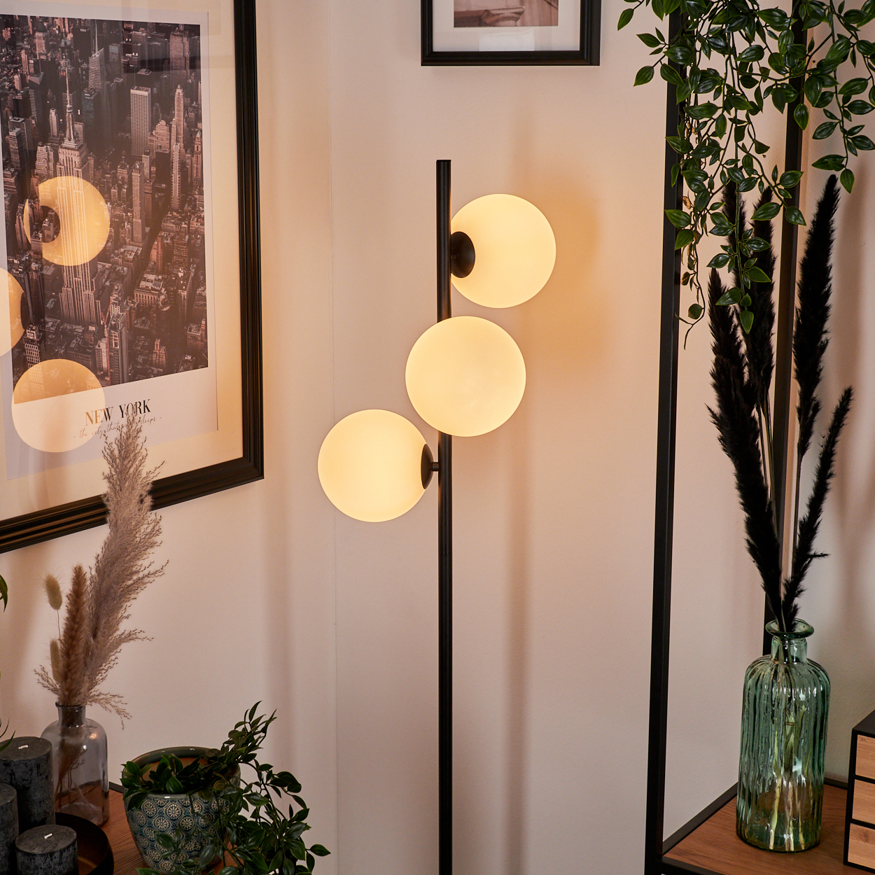 Ein modernes Wohnzimmer mit einer Stehlampe mit drei Kugelleuchten, einem New York-Poster und dekorativen Pflanzen.