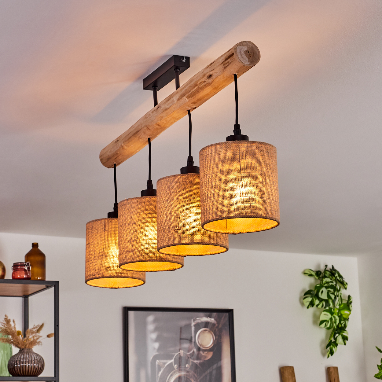 Ein Holzbalken mit vier zylindrischen Lampenschirmen hängt von der Decke. Die Lampenschirme sind beige und das Licht scheint hindurch.