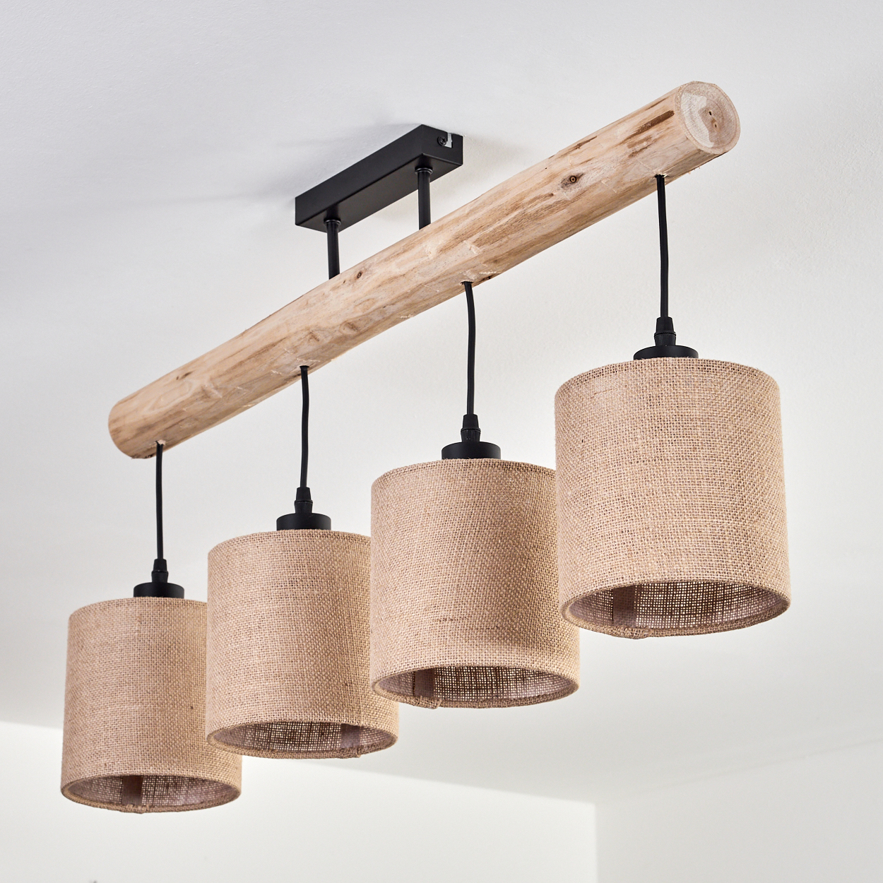 Ein Holzbalken mit vier Lampen aus beigem Stoff hängt von einer weißen Decke. Schwarze Kabel und Armaturen verbinden die Lampen.