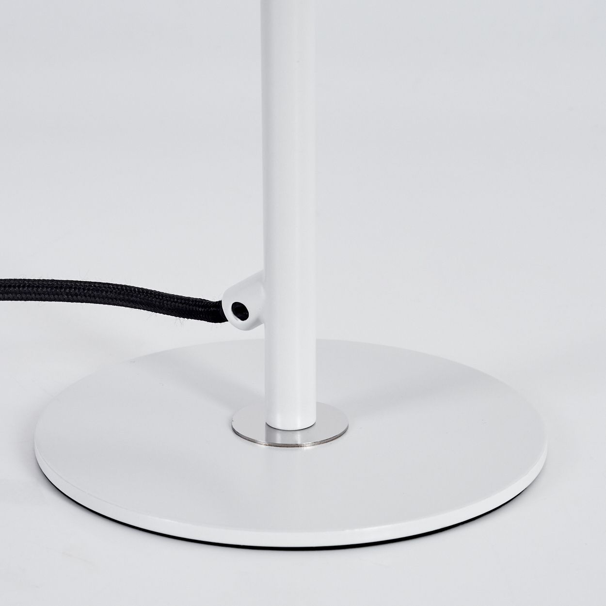 Ein weißer Lampenfuß mit kreisförmiger Basis und Stiel. Ein schwarzes Kabel ist am Stiel befestigt. Der Hintergrund ist schlicht weiß.