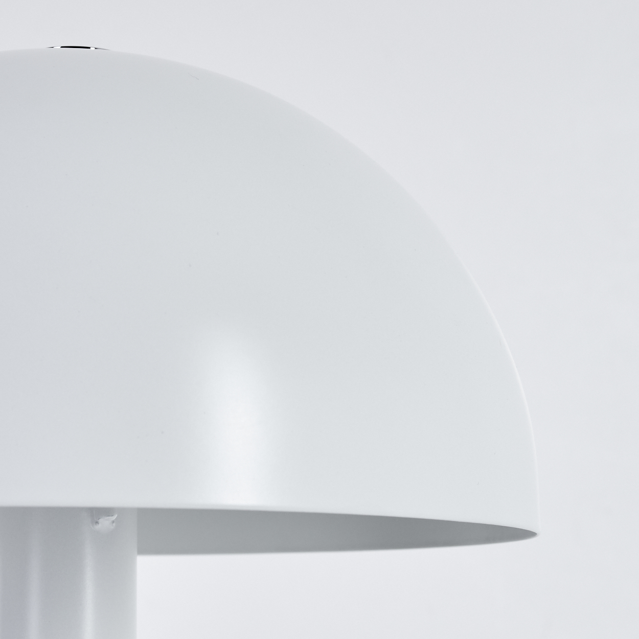Nahaufnahme einer weißen pilzförmigen Lampe. Die Lampe hat eine abgerundete Oberseite und einen zylindrischen Sockel, vor weißem Hintergrund.