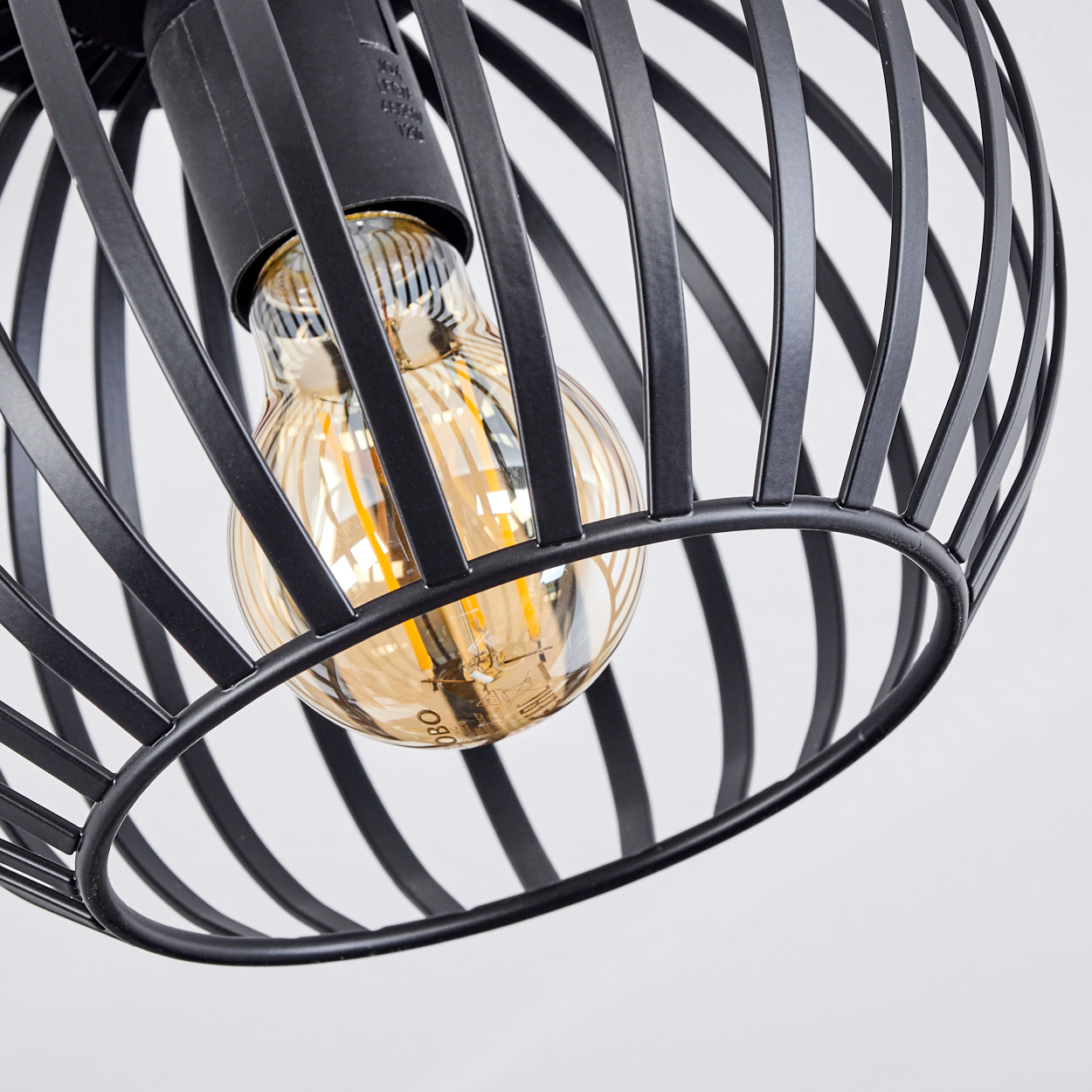 Nahaufnahme einer schwarzen Metallkäfig-Lichtvorrichtung mit einer warm getönten Glühbirne. Der Hintergrund ist weiß.