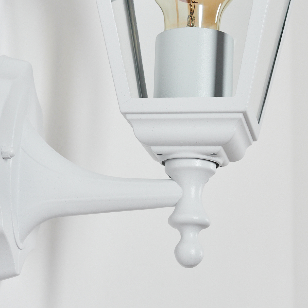 Eine weiße Außenlampe ist an einer weißen Wand montiert. Sie hat ein Glasgehäuse und eine Glühbirne. Die Lampe ist elegant.