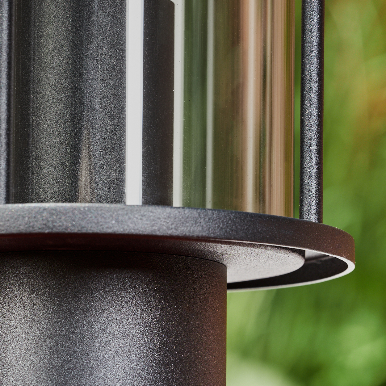 Nahaufnahme einer schwarzen Metalllampe. Zylindrische Abschnitte mit Glas. Verschwommener grüner Hintergrund mit Blättern.