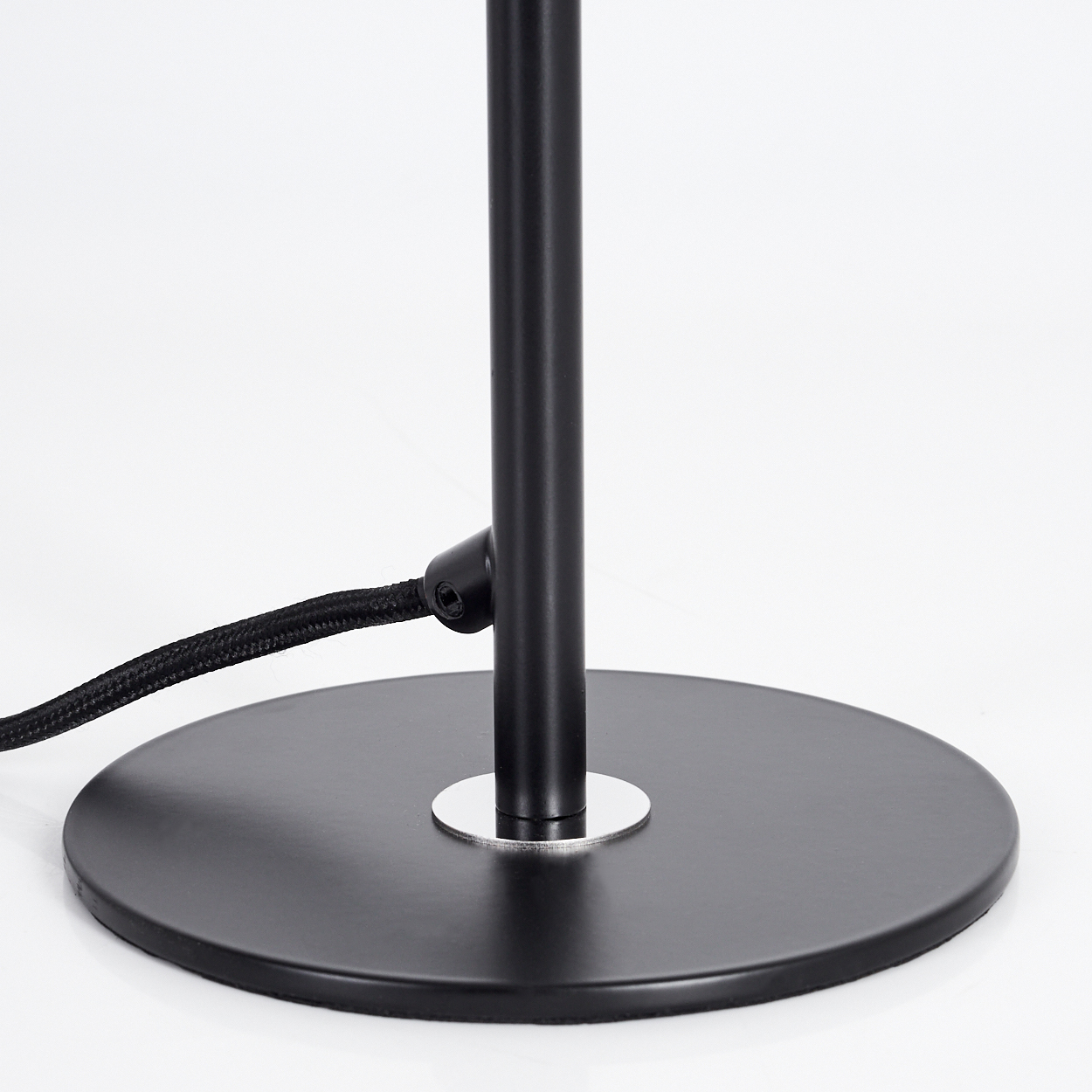 Nahaufnahme eines schwarzen Lampenfußes auf weißer Oberfläche. Ein schwarzes Kabel ist mit dem Sockel verbunden. Der Schaft der Lampe ist ebenfalls schwarz.