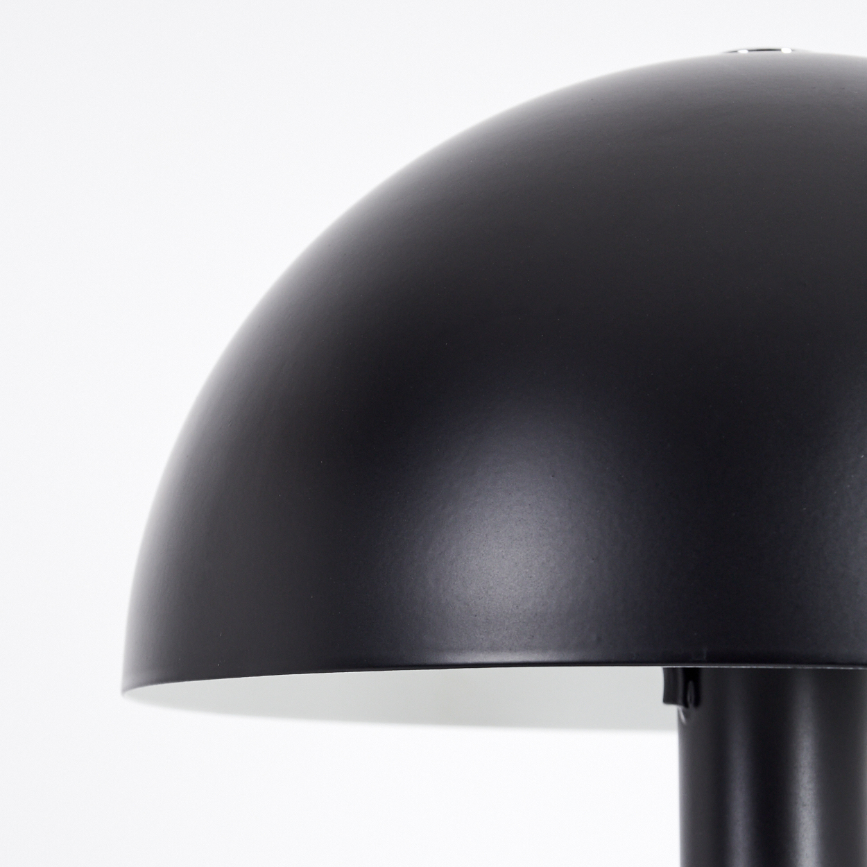 Nahaufnahme einer schwarzen Lampe. Der Lampenschirm ist kuppelförmig, mit weißem Innenraum und schwarzem Äußeren. Der Hintergrund ist weiß.