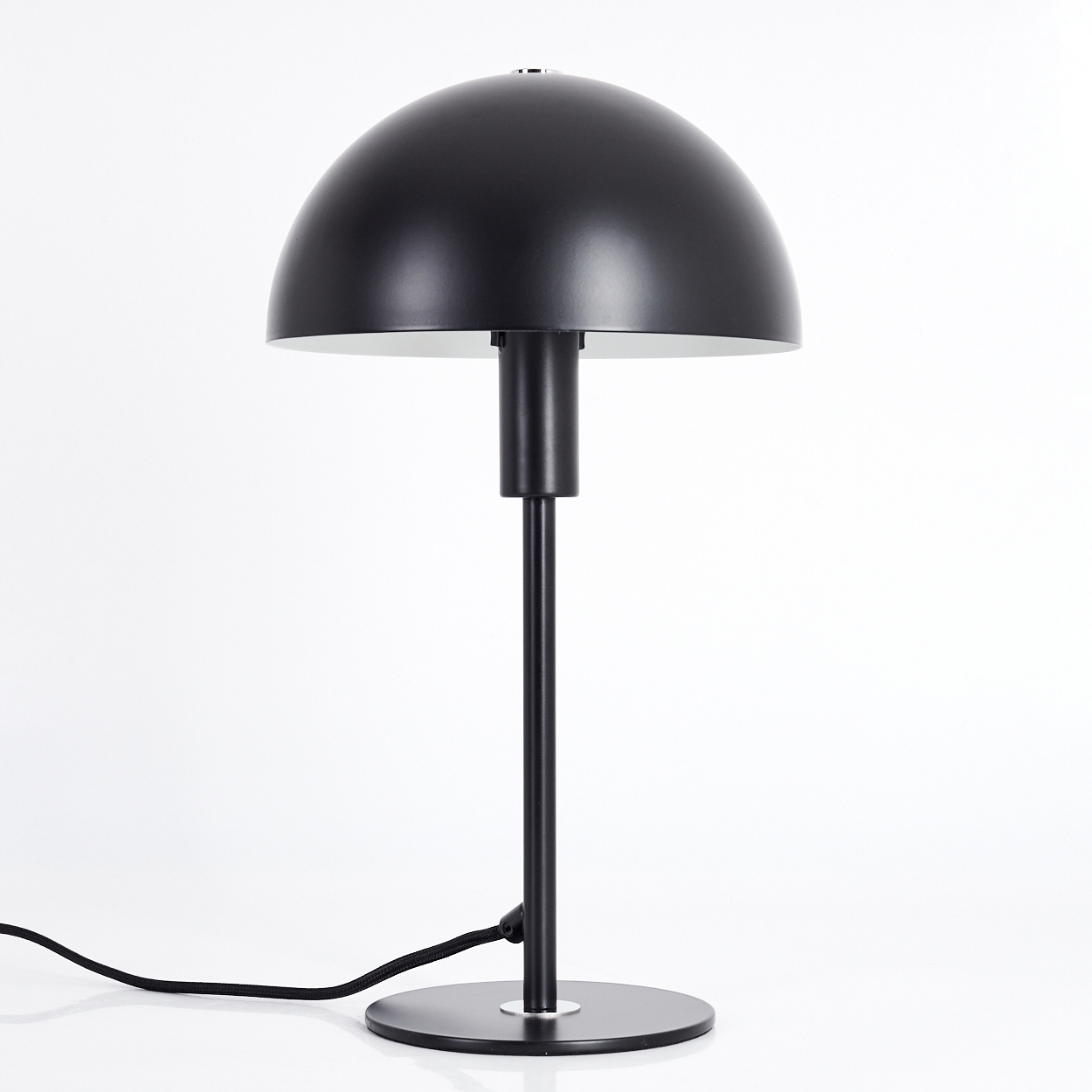 Eine schwarze Schreibtischlampe mit rundem Schirm und dünnem Stiel. Sie steht auf einem kreisförmigen Sockel mit schwarzem Kabel. Der Hintergrund ist weiß.
