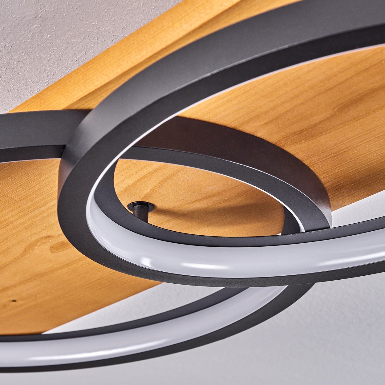 Nahaufnahme einer modernen Deckenleuchte. Sie hat einen Holzsockel, schwarze Metallringe mit weißen LED-Leuchten und eine weiße Decke.