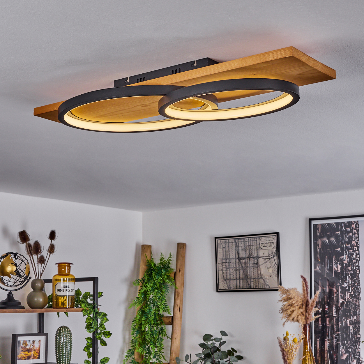 Deckenlampe mit zwei kreisförmigen Lampen auf Holzsockel. Raum mit Deko, Regal, Leiter, Pflanzen und gerahmter Kunst.