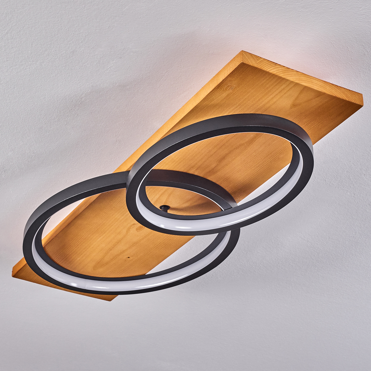Eine Deckenleuchte mit zwei schwarzen, kreisförmigen Lichtern auf einem Holzbrett. Der Hintergrund ist eine weiße Decke.