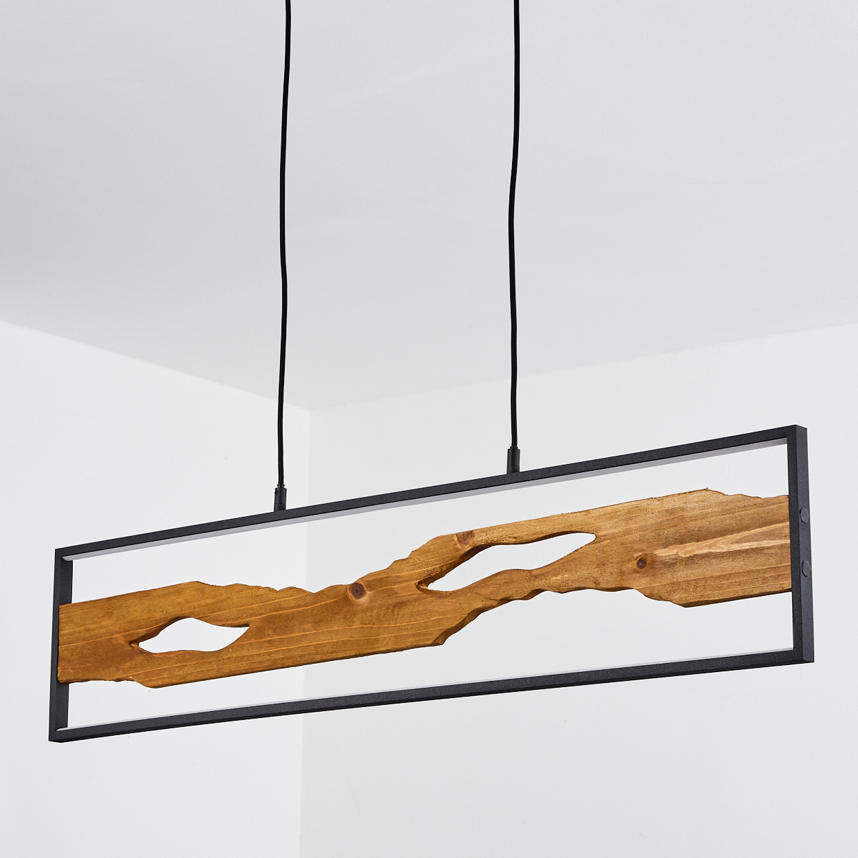 Eine rechteckige Holzlampe mit schwarzem Metallrahmen hängt an zwei schwarzen Kordeln. Das Holz hat eine natürliche, unregelmäßige Form mit Aussparungen.