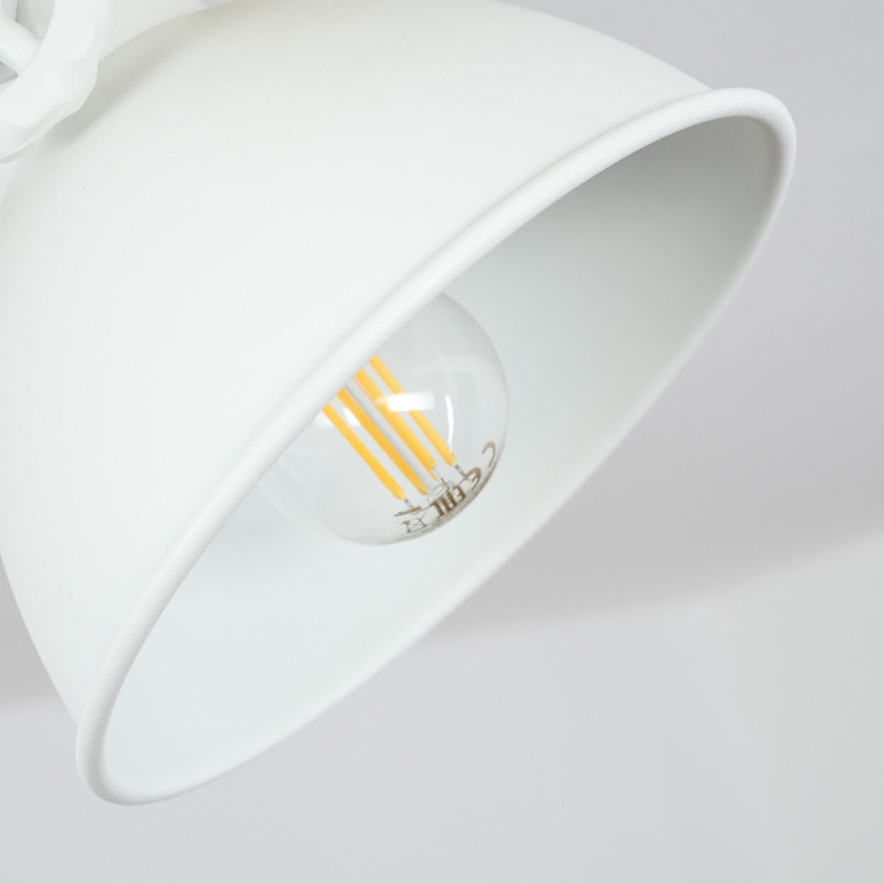 Eine weiße Lampe mit gebogenem Schirm, eine klare Glühbirne mit gelben Filamenten und ein weißer Hintergrund.