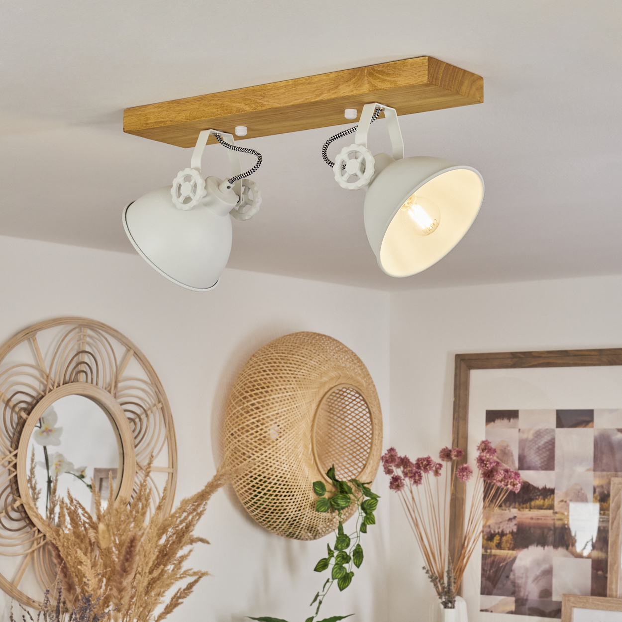Zwei weiße Strahler an einem Holzbalken an der Decke. Dekorative Elemente an der Wand sind Spiegel und ein geflochtener Korb.