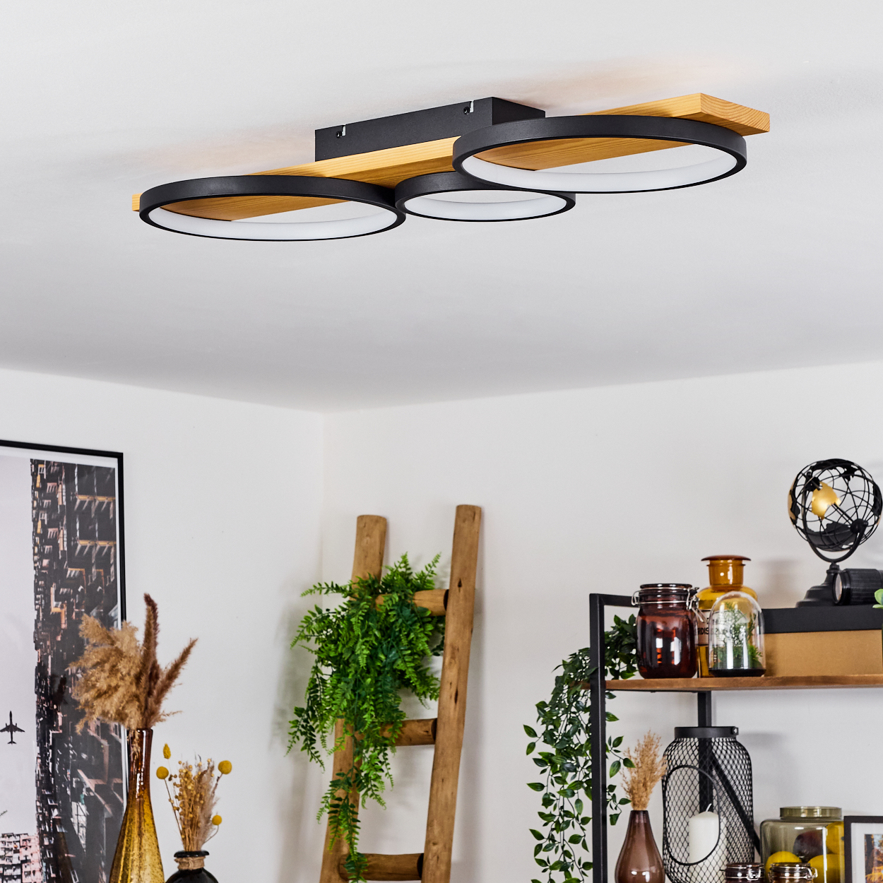 Eine moderne Deckenlampe mit drei schwarzen und weißen kreisförmigen Lichtern. Darunter ein Raum mit Regalen, einer Holzleiter und Dekorationsartikeln.