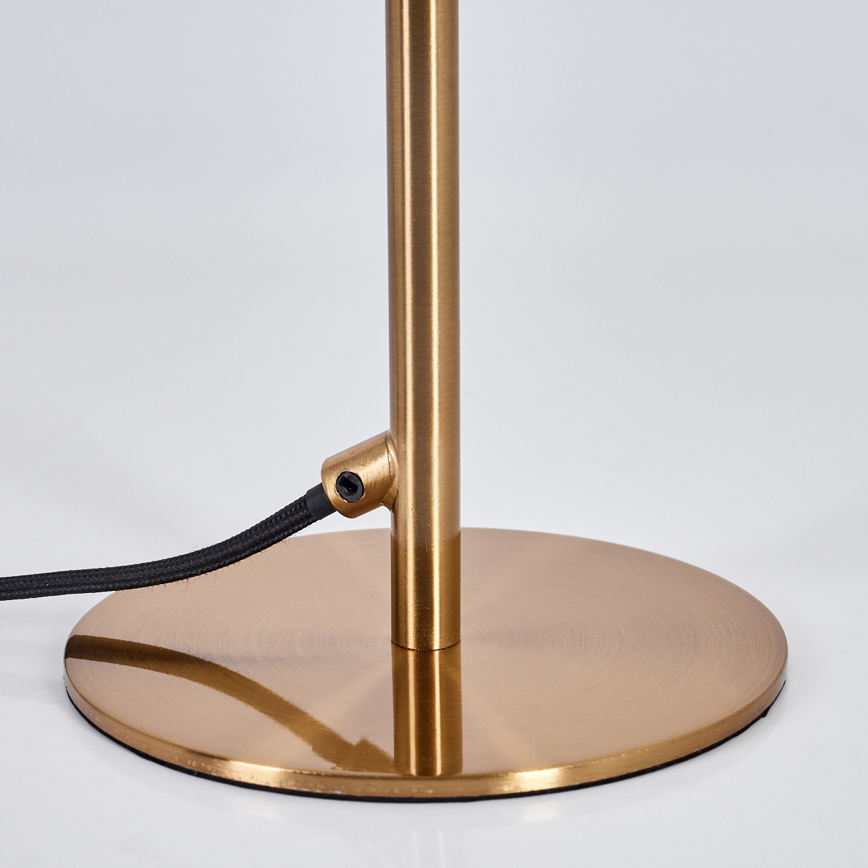Nahaufnahme eines goldenen Lampenfußes und -stiels. Ein schwarzes Kabel kommt aus der Seite des Stiels. Der Fuß ist eine kreisförmige Scheibe.