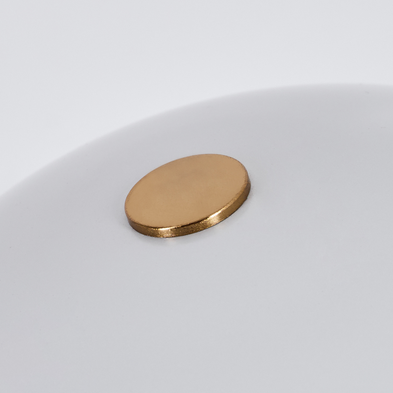 Nahaufnahme einer weißen, gekrümmten Oberfläche mit einem goldfarbenen, ovalförmigen Detail in der Mitte. Das Detail hat einen leicht erhöhten Rand.