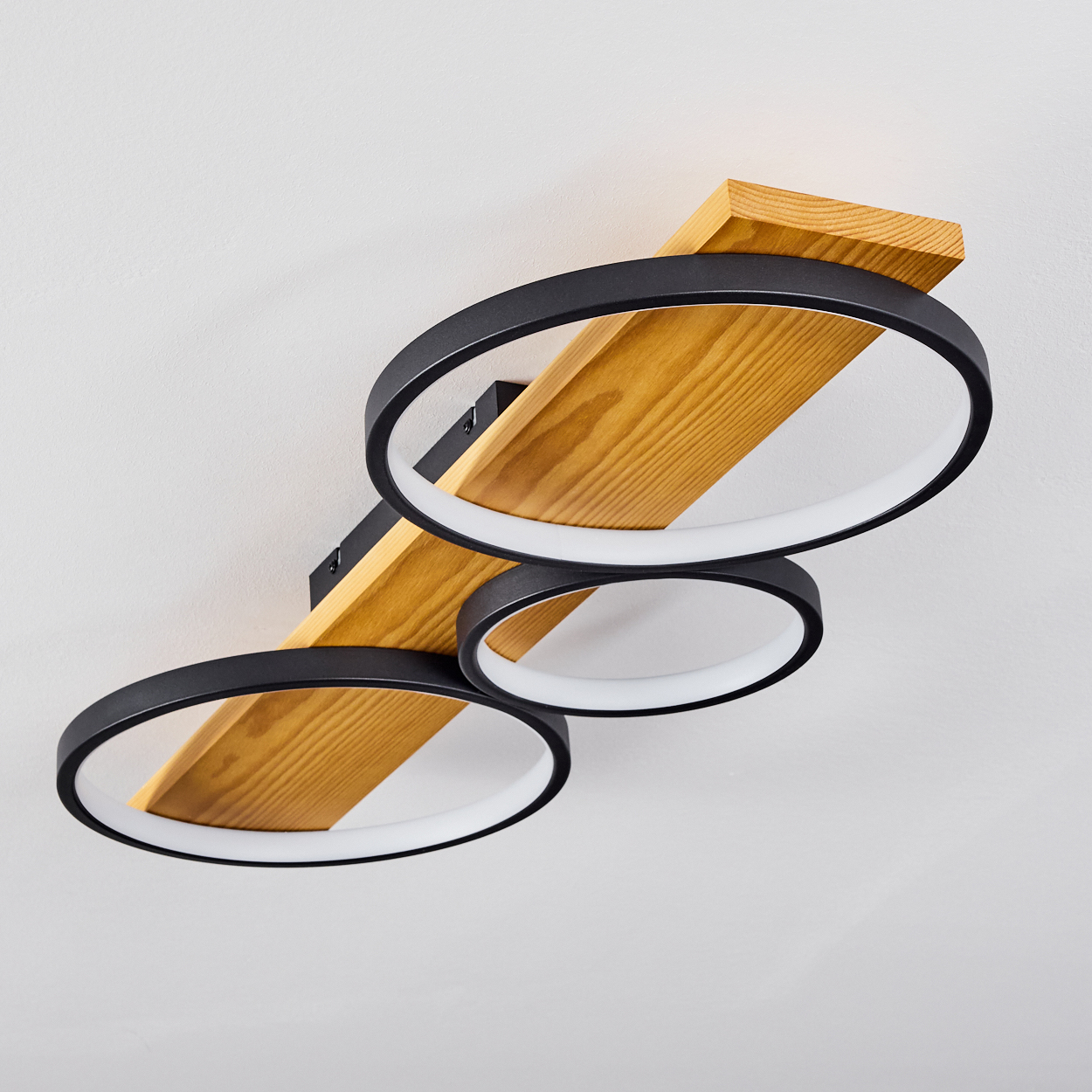 Moderne Deckenlampe mit drei schwarzen kreisförmigen Lichtern und einem Holzbalken, an einer weißen Decke installiert.