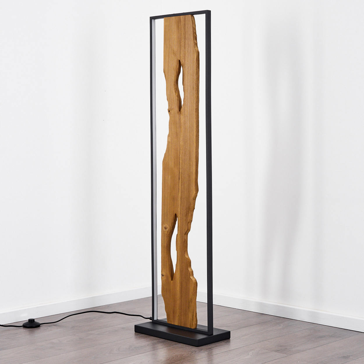 Holzlampe mit schwarzem Rahmen, die auf einem Holzboden steht. Ein Stromkabel und eine weiße Wand sind im Hintergrund.