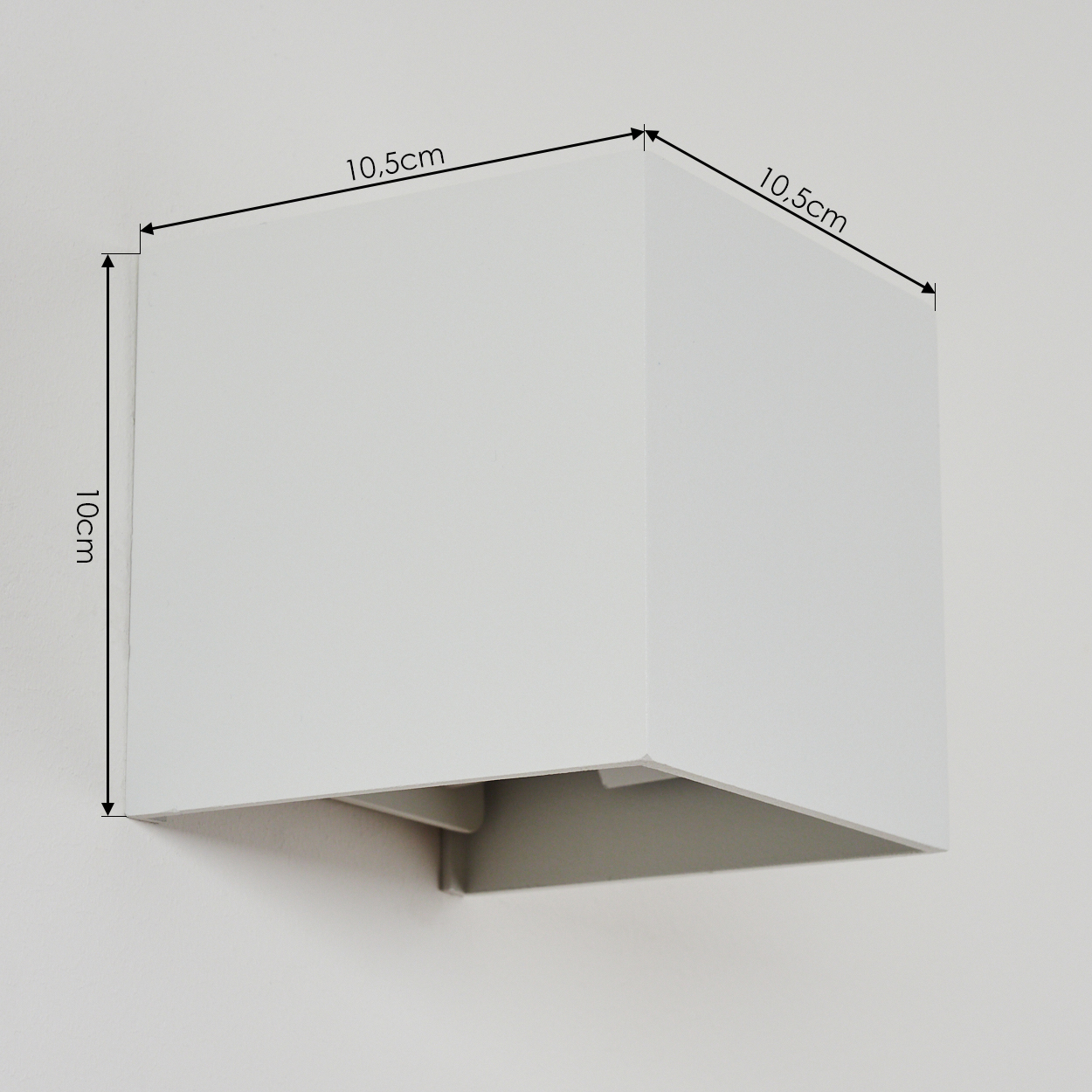 Eine weiße, würfelförmige Wandleuchte ist an einer weißen Wand montiert. Abmessungen sind 10 cm x 10,5 cm. Die Unterseite ist offen mit grauem Innenraum.