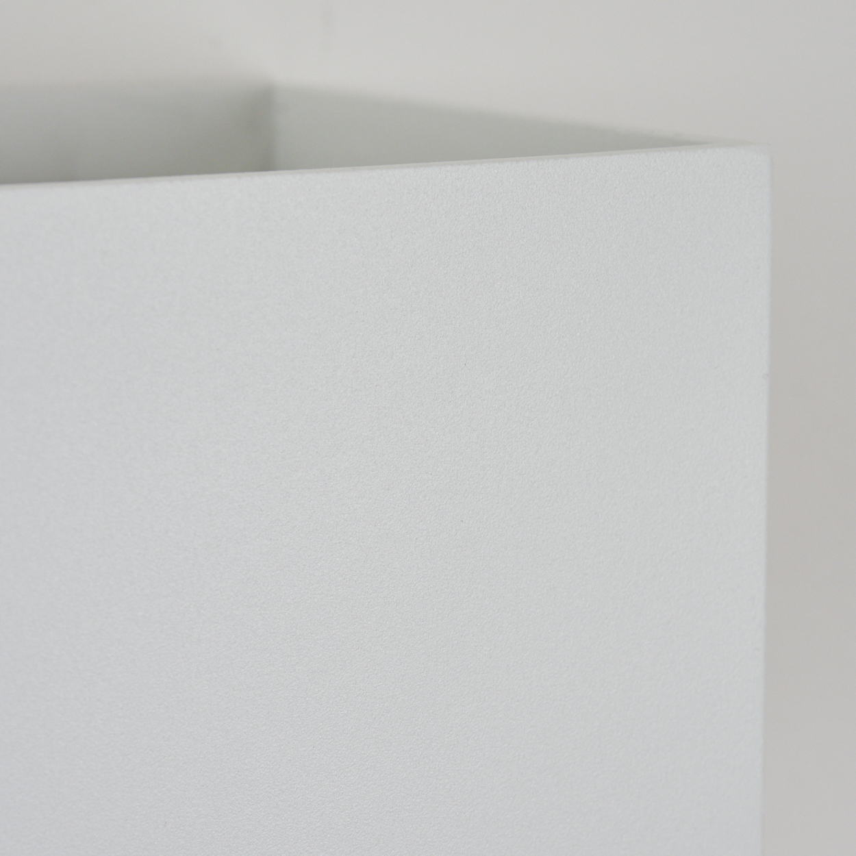 Nahaufnahme einer weißen, strukturierten Oberfläche, möglicherweise eine Wand oder eine Box. Die Ecke ist sichtbar, mit hellem Hintergrund.